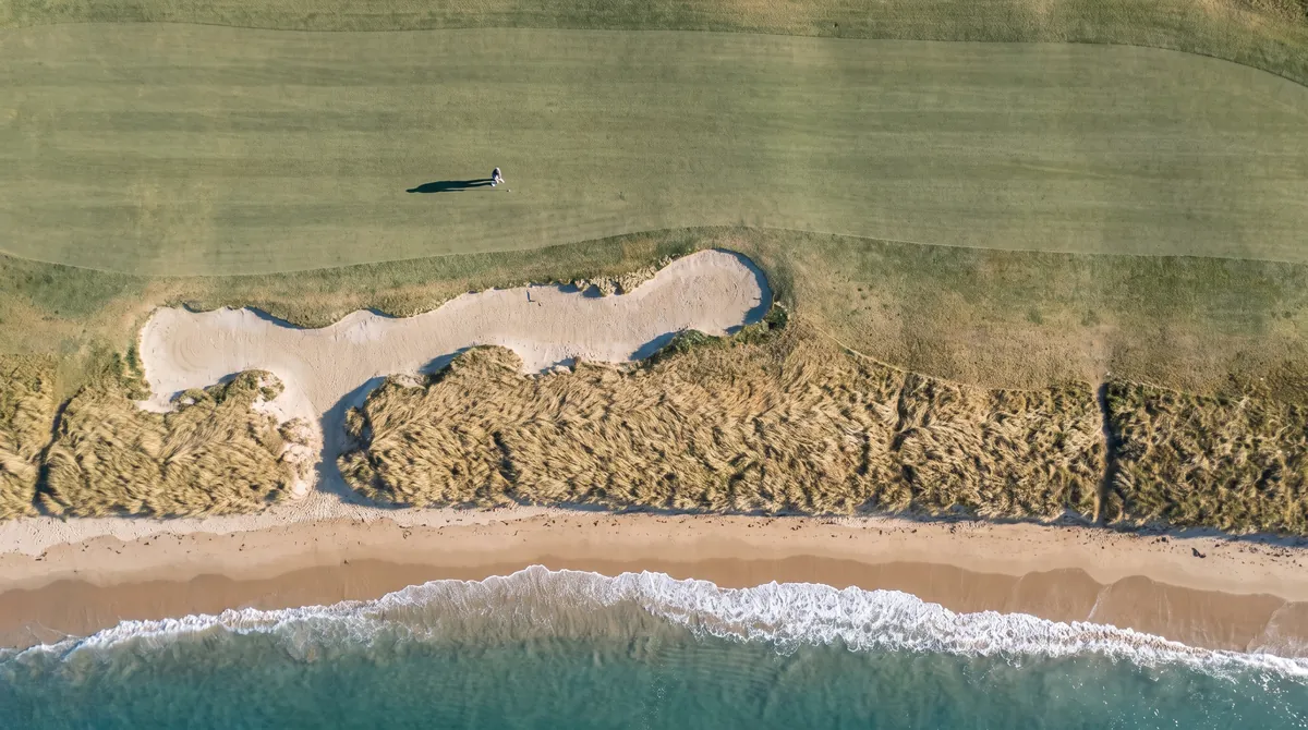 Seen from directly above: fairway, bunker, fescue, beach and surf.