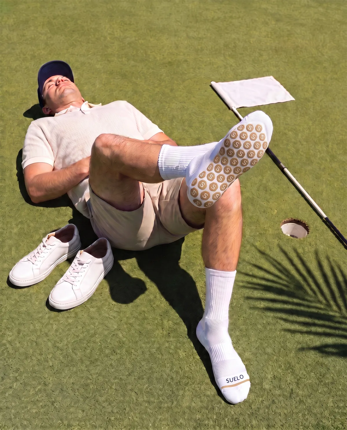 A golfer lies on a green, one foot crossed over a knee so the sock's grip sole faces up.