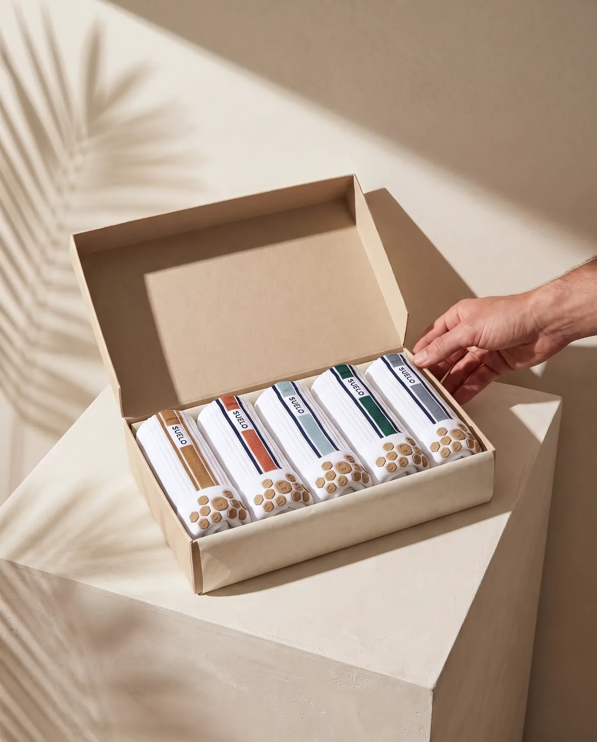 An open box holding five rolled pairs of Suelo socks, each in a different colourway.